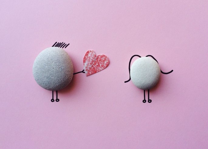 Stick figures made of rocks, one giving a heart to the other